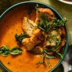 heirloom tomato soup in a bowl with fresh herbs, croutons, and spoons