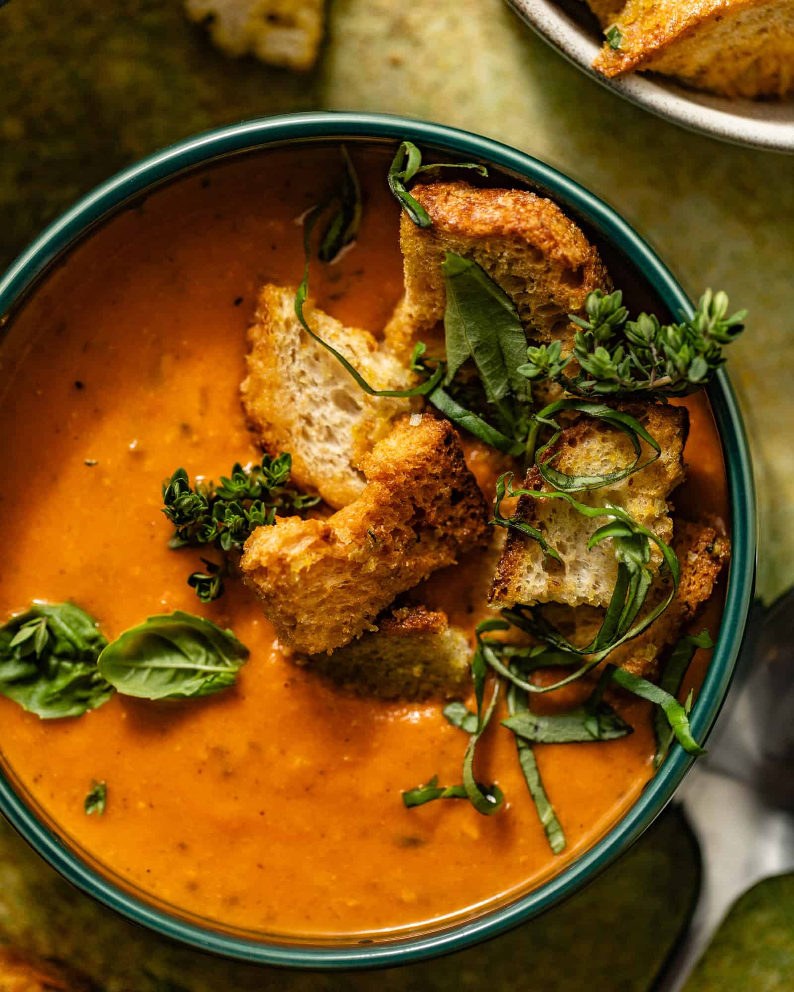 heirloom tomato soup in a bowl with fresh herbs, croutons, and spoons