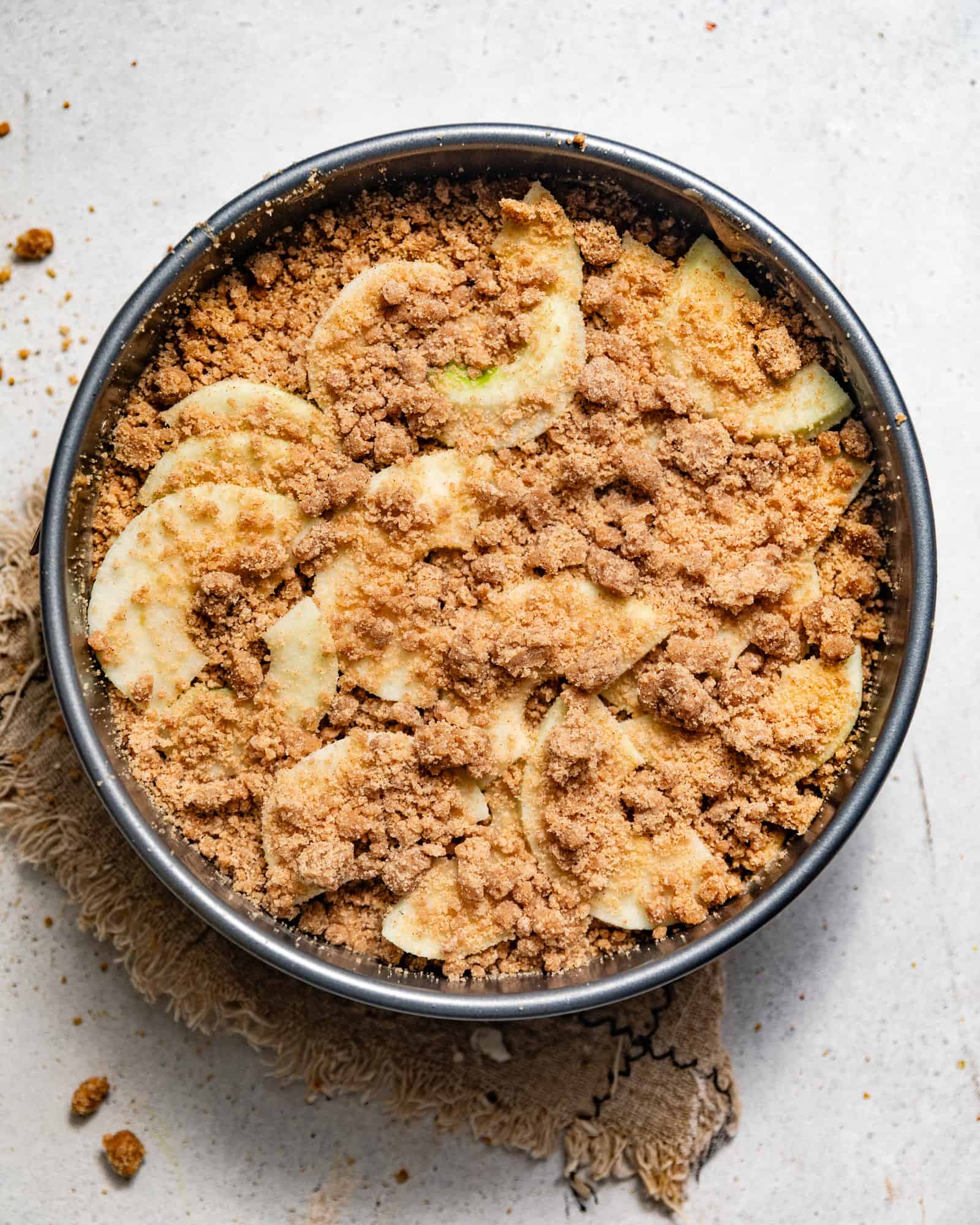 apple cake batter in a springform pan with a streusel topping and sliced apples
