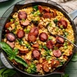 cajun orzo topped with sausage, fresh basil, and diced green onions in a skillet.