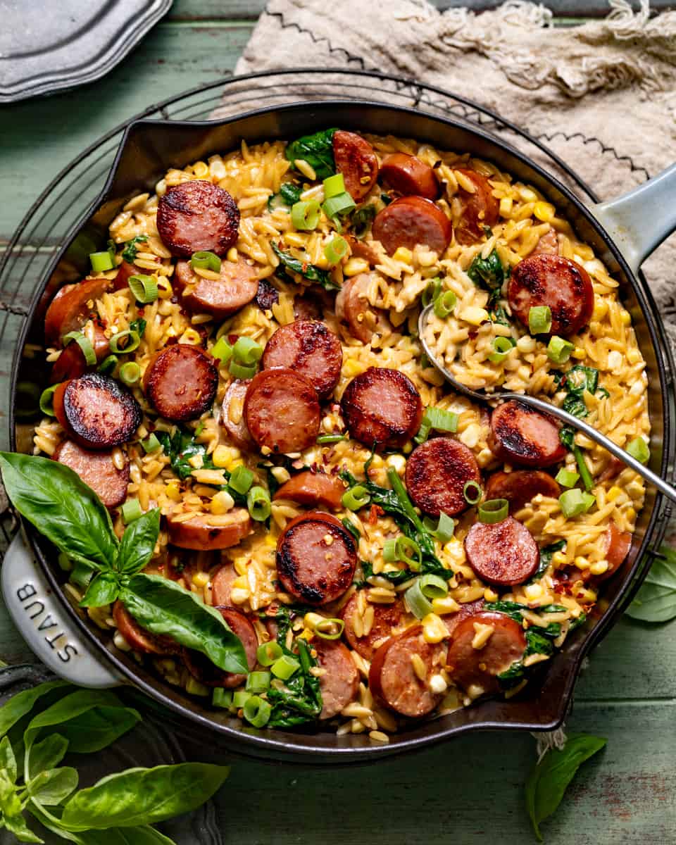 cajun orzo topped with sausage, fresh basil, and diced green onions in a skillet.