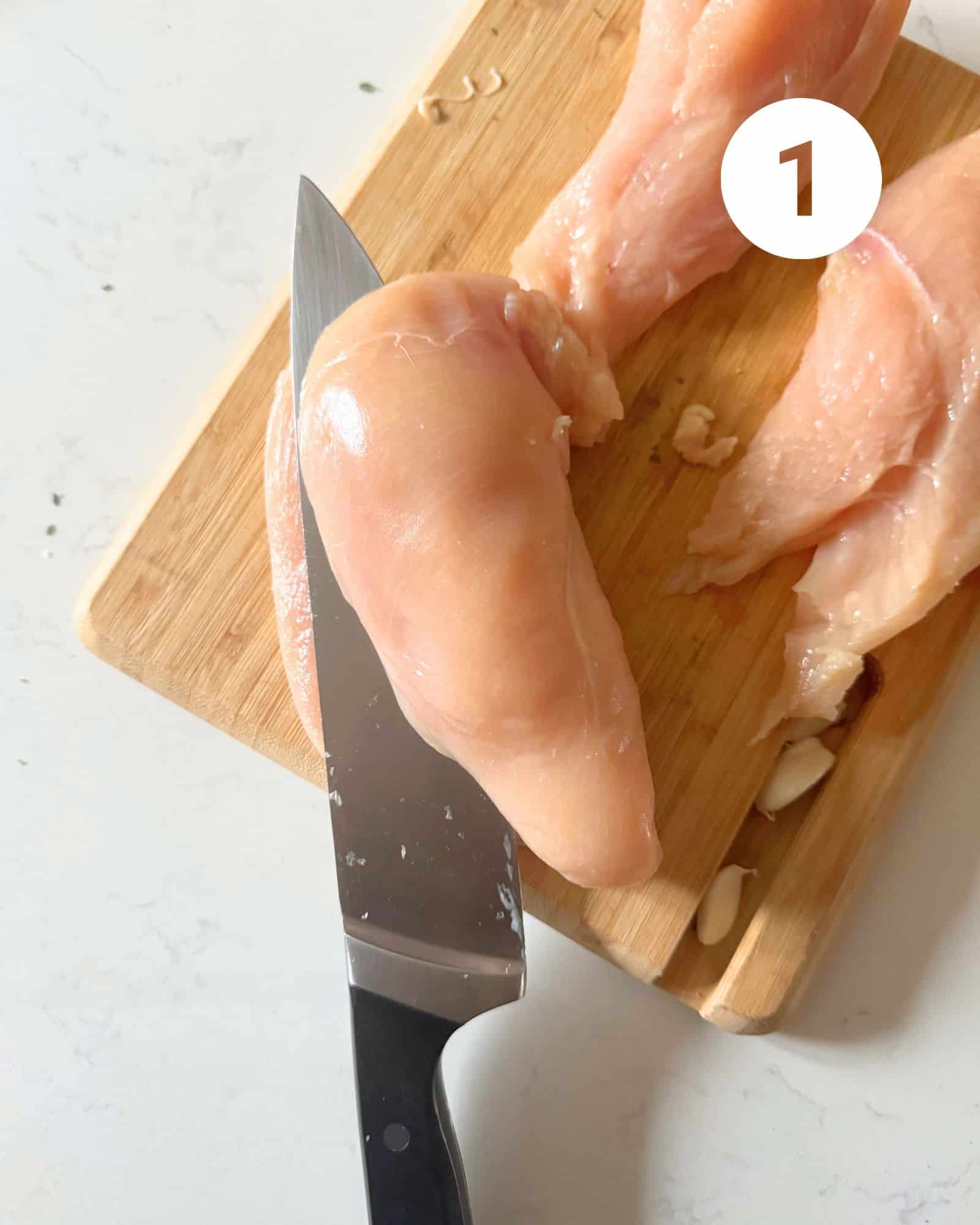 a photo of a knife cutting a piece of chicken breast in half.