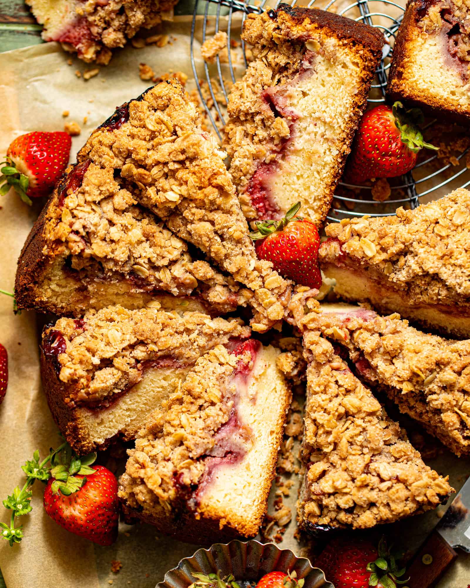 slices of strawberry crumb cake on top of parchment paper with fresh strawberries and a butter knife.