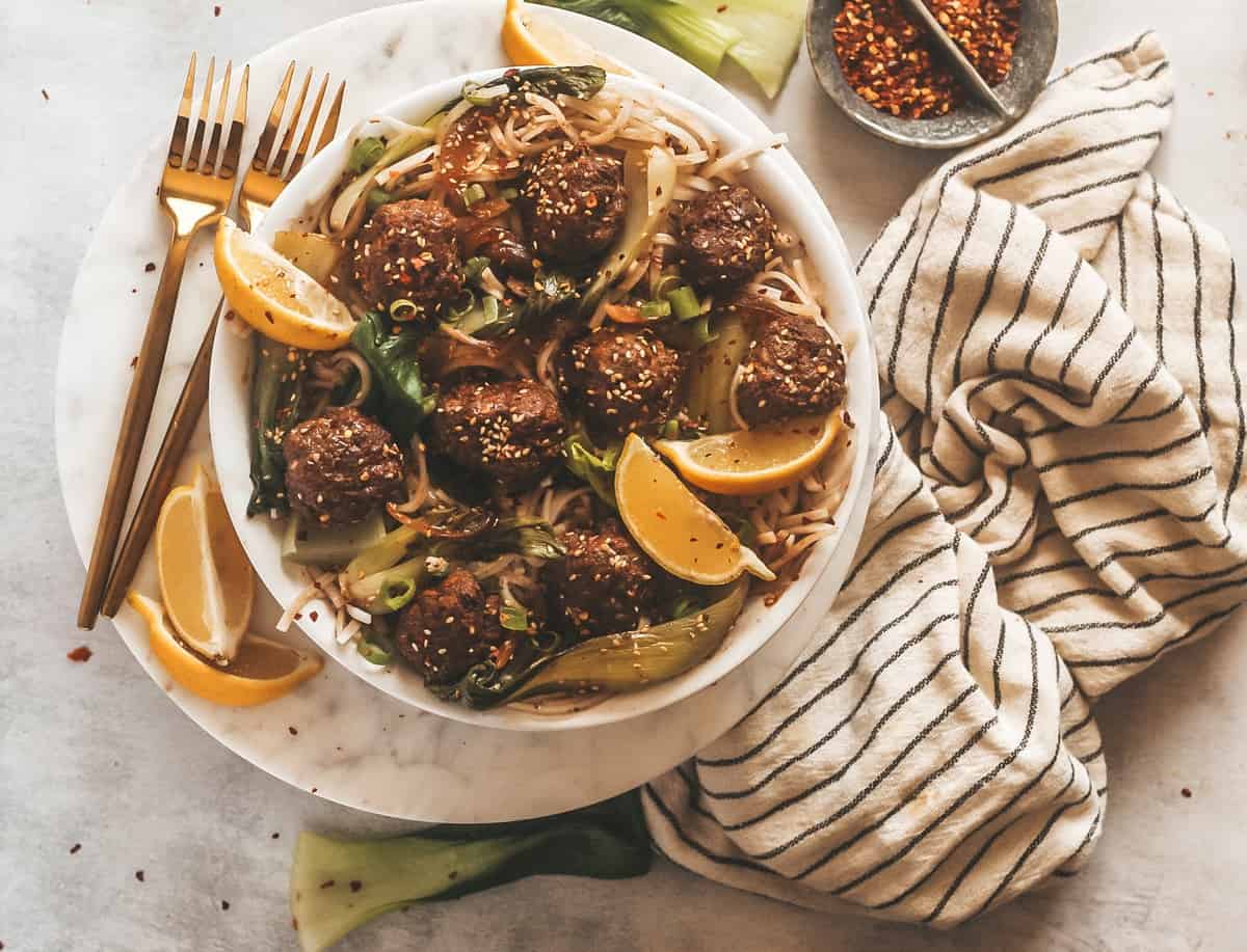 swedish meatballs in a bowl with noodles and garnished with sliced lemons.