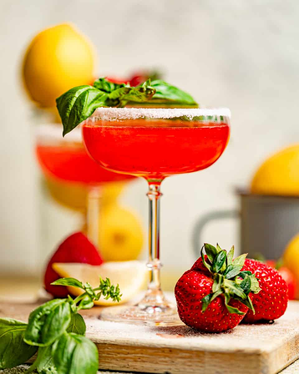 strawberry lemon drop martini in a martini glass with a sugar rim garnished with fresh basil.