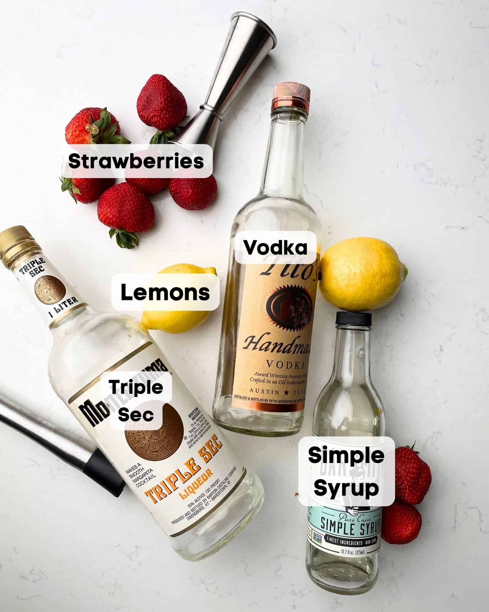 ingredients to make a strawberry lemon drop on a white surface - strawberries, lemons, vodka, triple sec, and simple syrup.