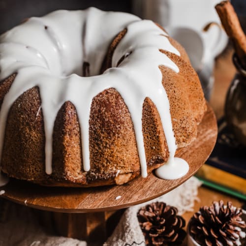 a spiced bundt cake on a cake stand with a cup of cinnamon sticks.