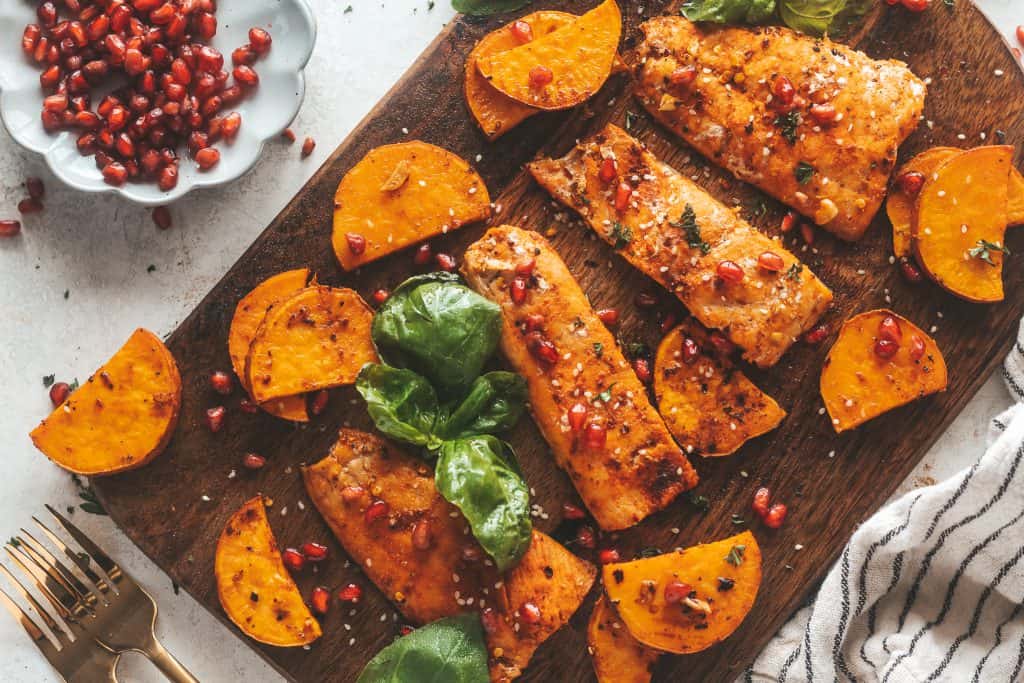 salmon on a cutting board with veggies and pomegranates