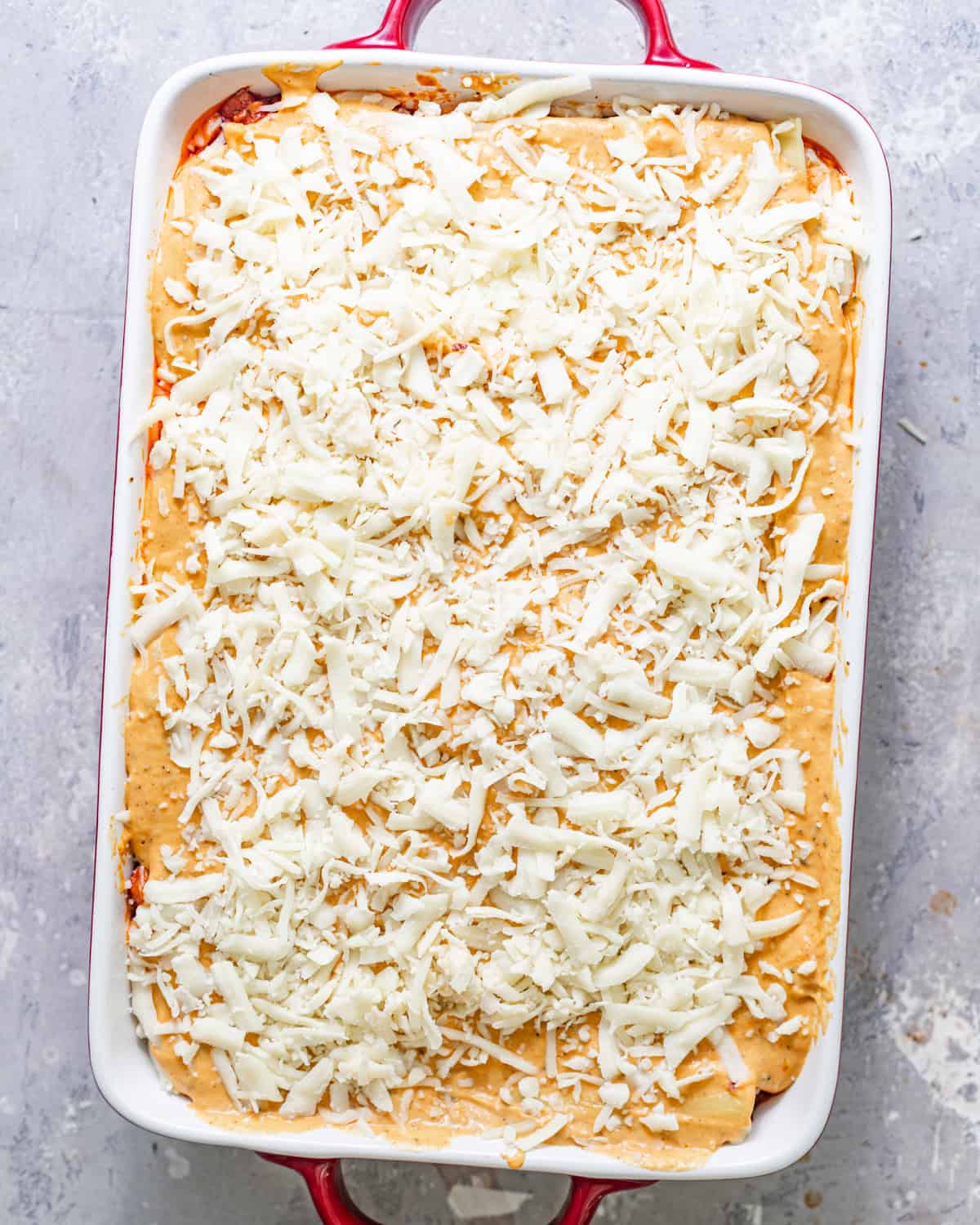 pumpkin lasagna assembled in a baking dish and topped with a generous amount of shredded cheese.