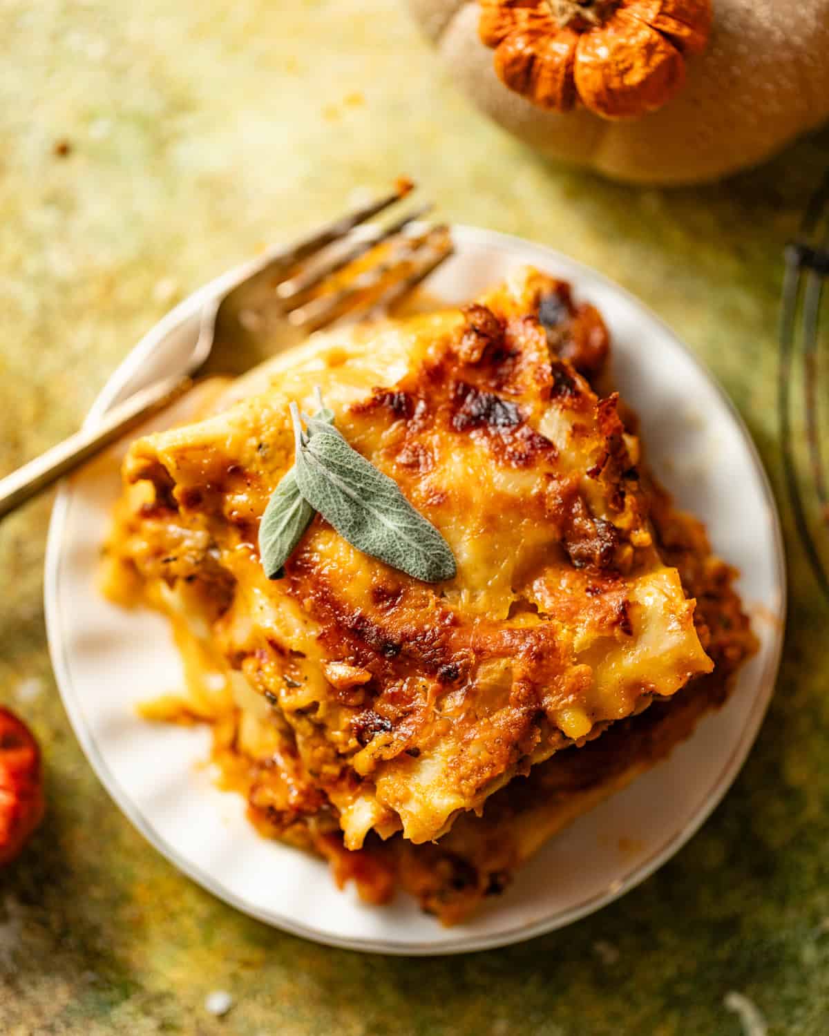 a slice of pumpkin lasagna on a plate topped with a sage leaf. 