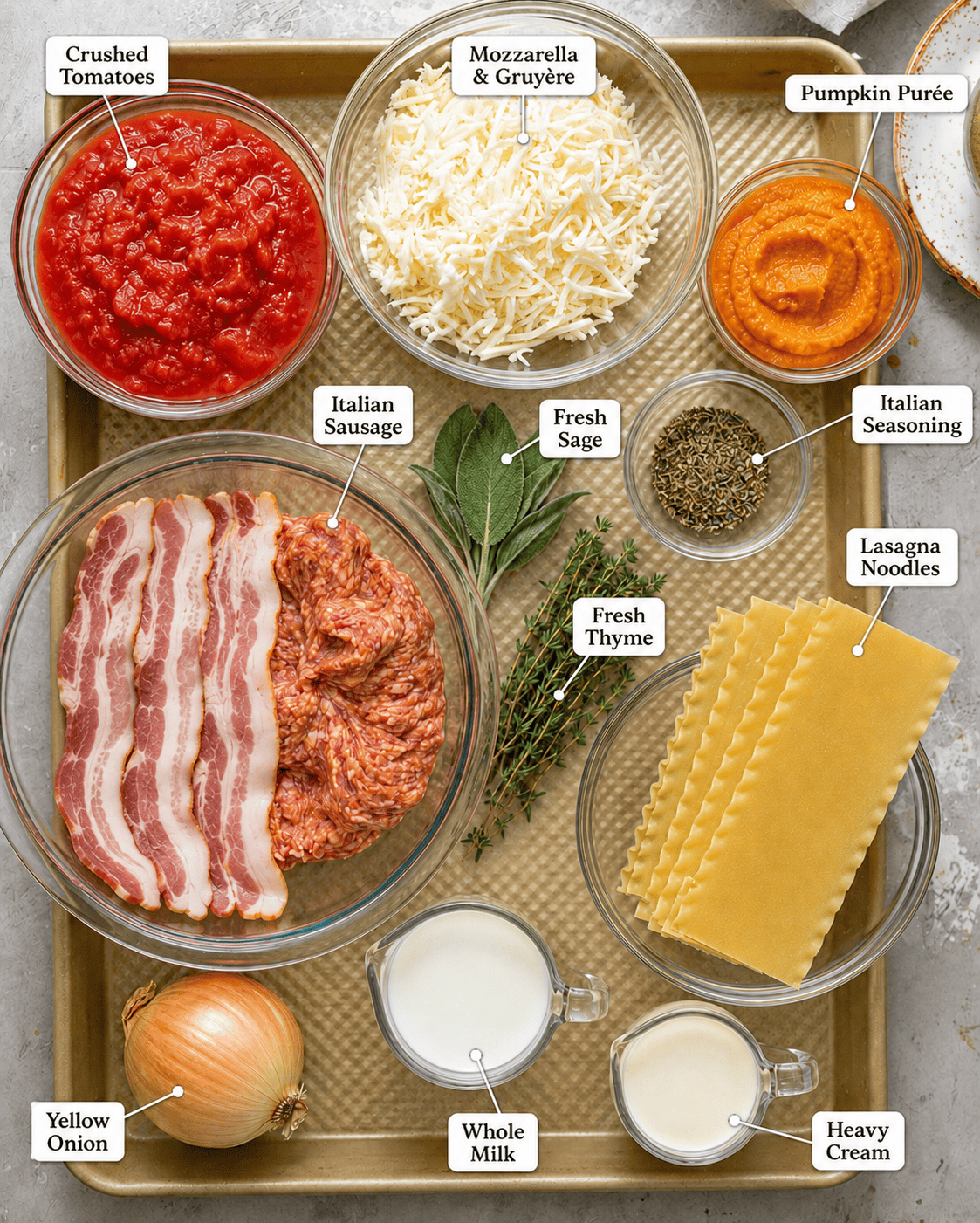 pumpkin lasagna ingredients on a baking sheet including pumpkin purée, Italian sausage, bacon, crushed tomatoes, herbs, cheese, whole milk, heavy cream, and lasagna noodles.