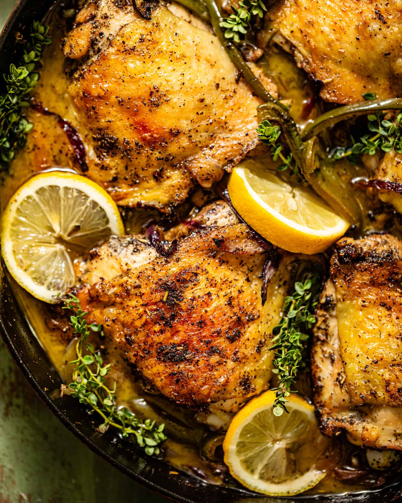an up close photo of skillet chicken thighs in a cast iron skillet with lemon, thyme, red onion, and garlic.