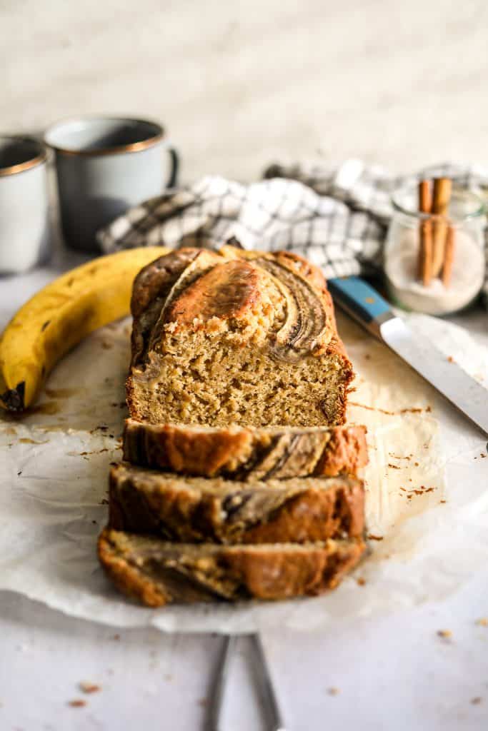 loaf sliced with a banana and cups behind it 