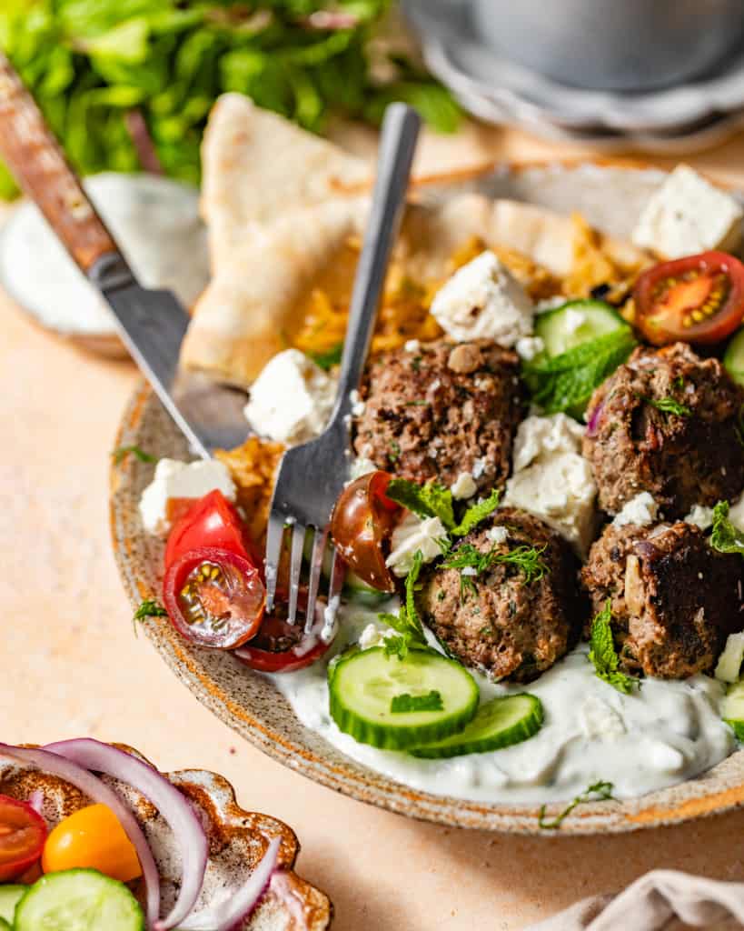 greek meatballs in a bowl with tzatziki sauce, tomatoes, and cucumbers.