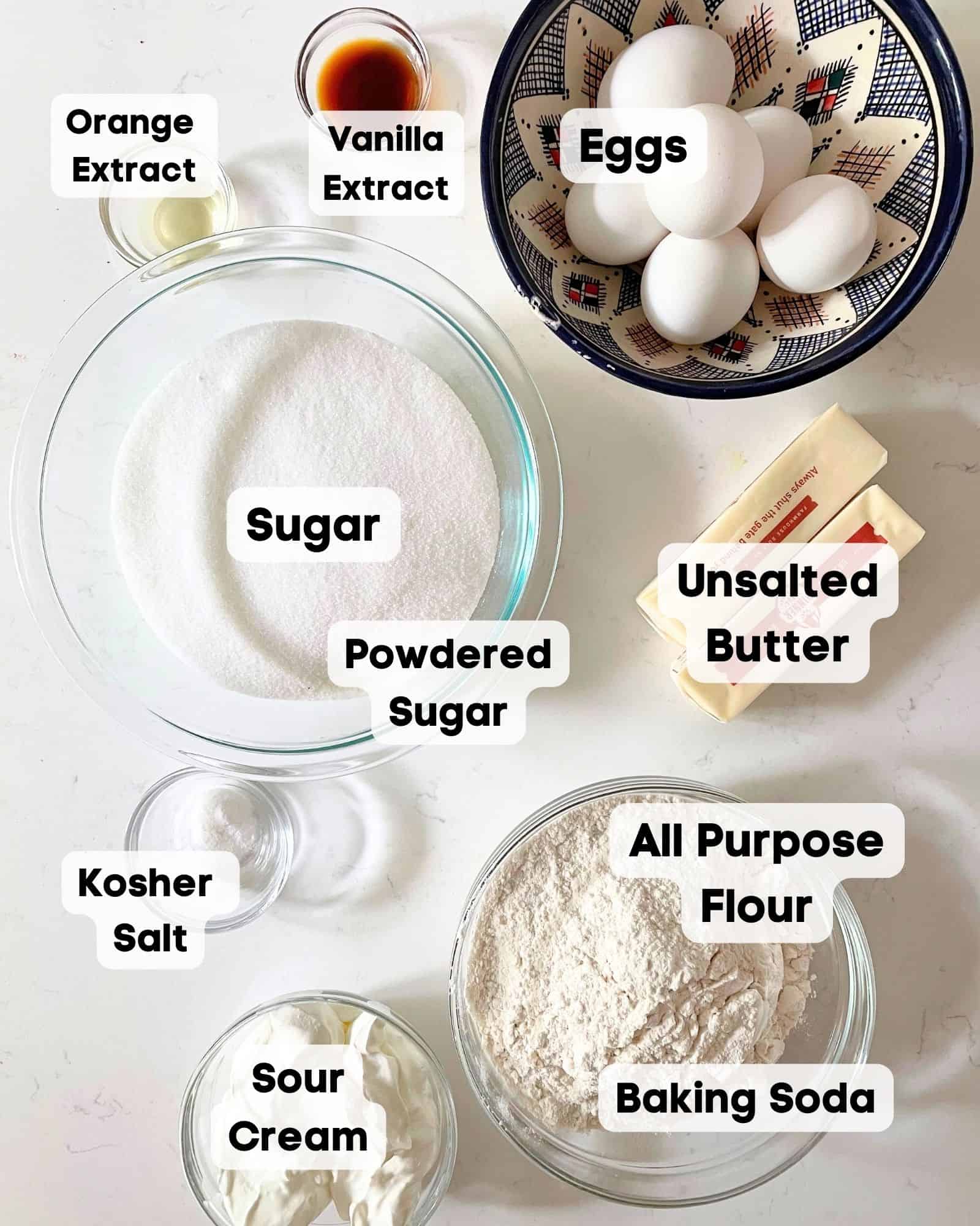 ingredients to make sour cream pound cake on a white surface placed in bowls.