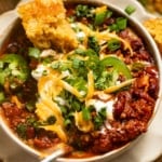up close photo of chili in a bowl with a spoon and topped with cilantro and cheese.