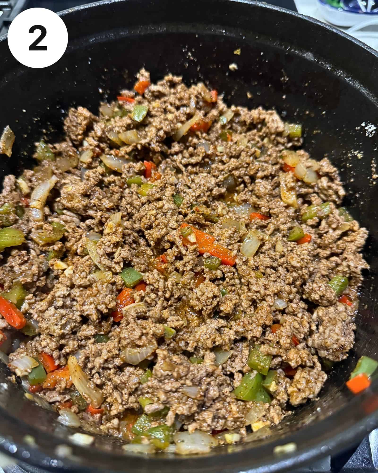 diced bell peppers, onions, garlic, and seasonings in a dutch oven with ground beef.