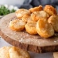 Pao De Queijo on a wooden cheese board with fresh herbs in the background