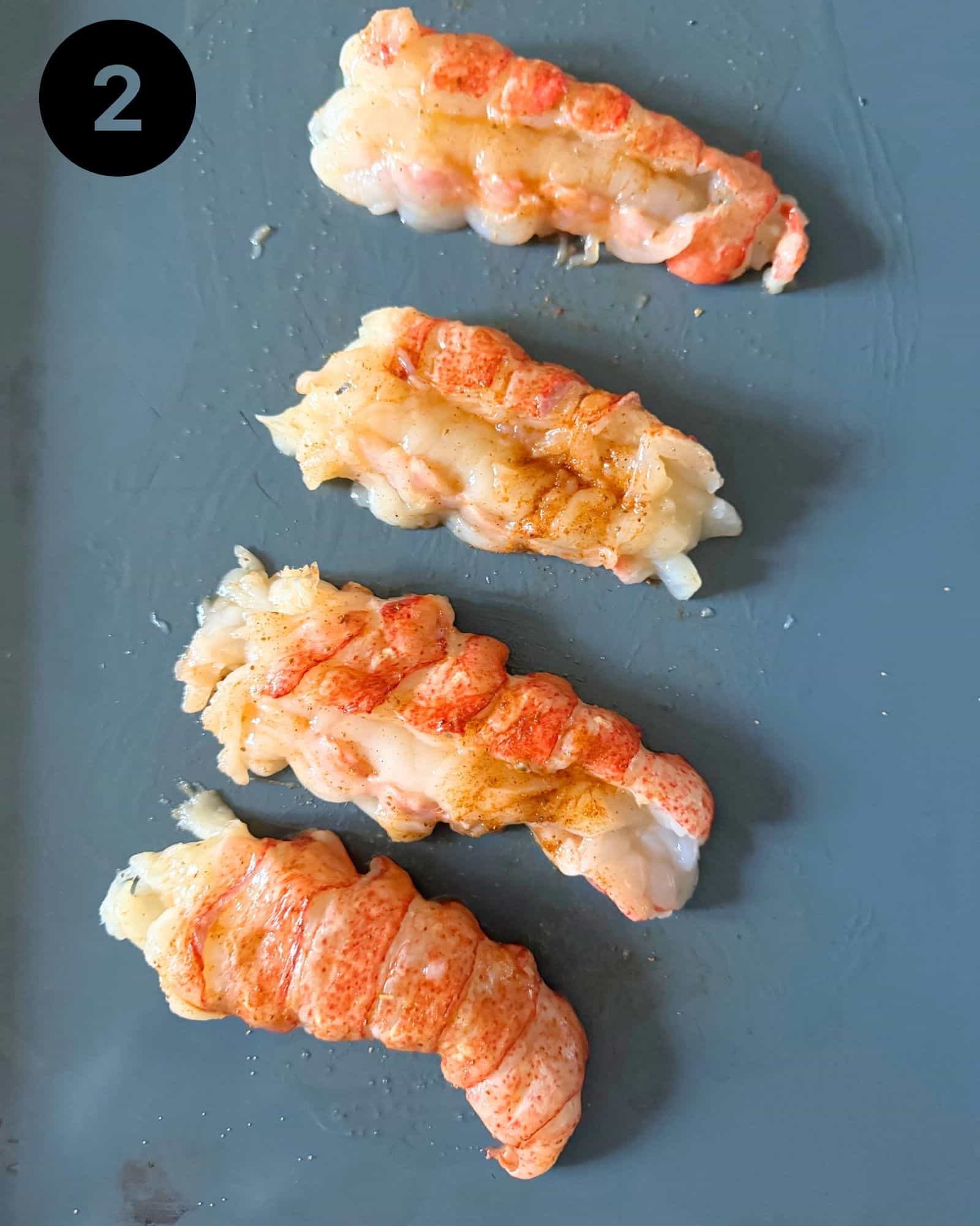 lobster tails on a baking sheet seasoned with old bay, pepper, and salt