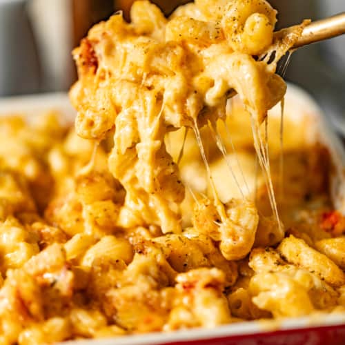 lobster mac and cheese in a casserole dish being scooped out onto a spoon so that you can see the cheese pull