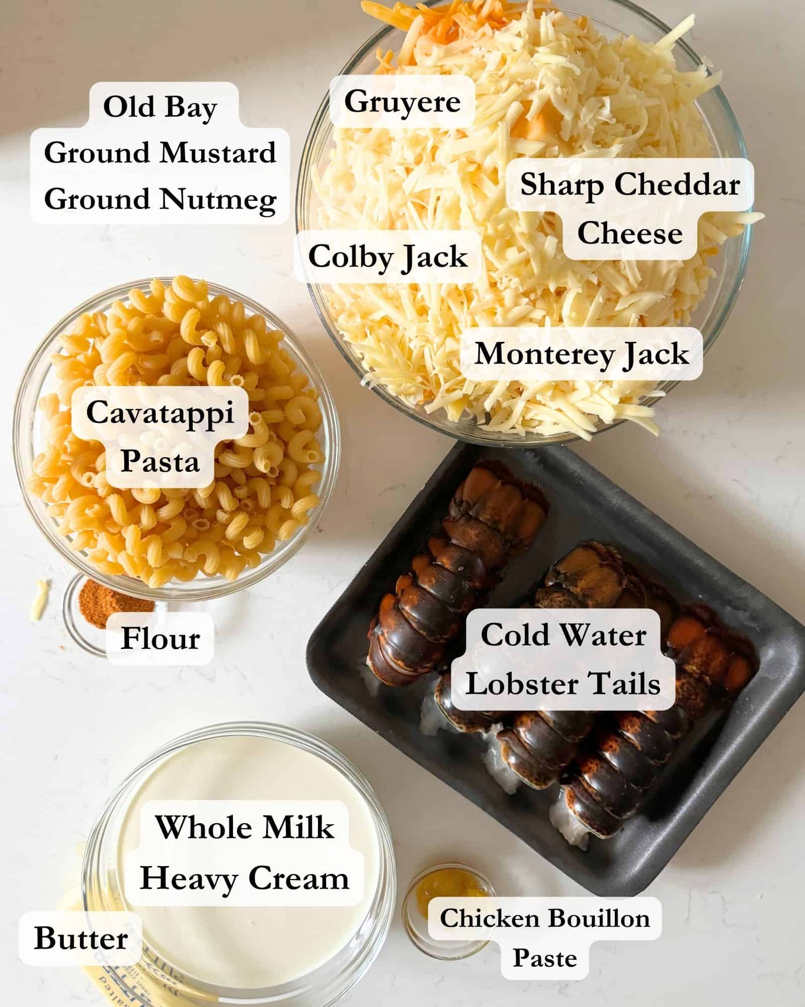 ingredients to make lobster mac and cheese on a white counter top in bowls - colby jack, gruyere cheese, monterey jack cheese, sharp cheddar cheese, lobster tails, pasta, seasonings, heavy cream, and whole milk