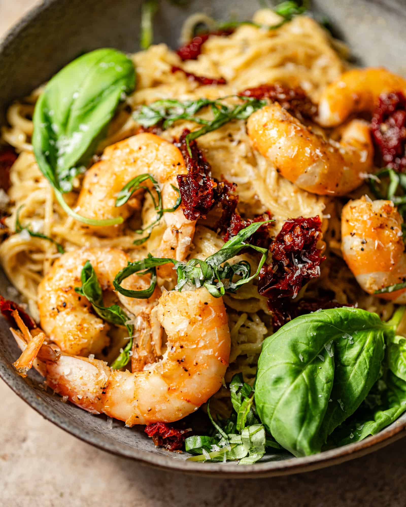 up close photo of pesto shrimp pasta in a bowl with sun-dried tomatoes and fresh basil