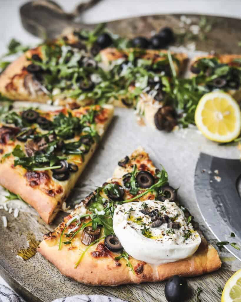 Cheesy Olive Pizza on a cutting board topped with arugula and burrata
