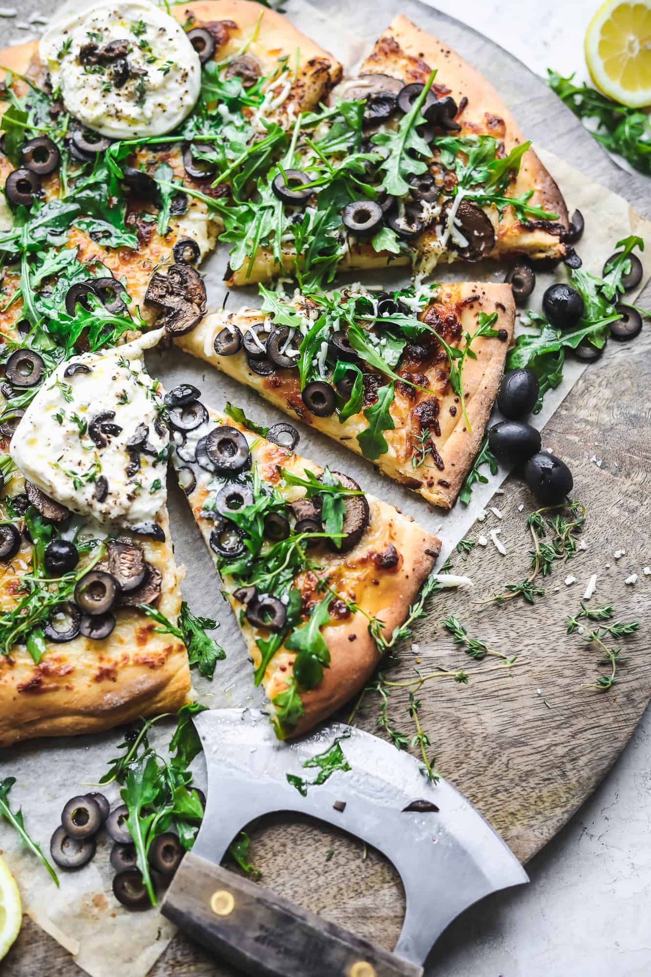 Cheesy Olive Pizza on a cutting board topped with arugula and burrata
