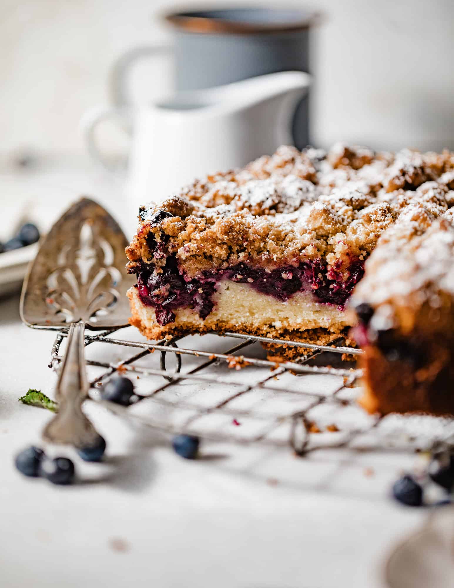 blueberry coffee cake on a wire rack with a cake server. 