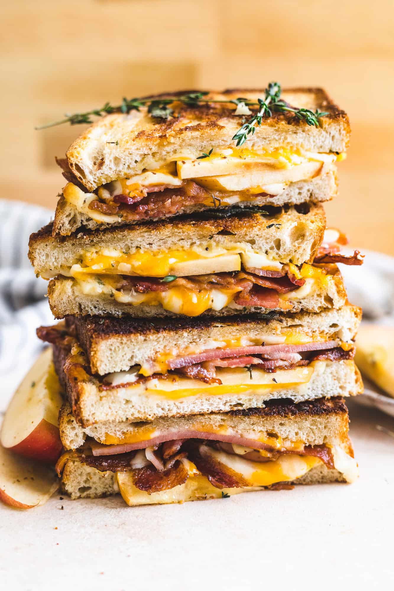 an apple bacon grilled cheese sandwich cut in half and stacked on top of each other with the cheese oozing out of the sandwich.
