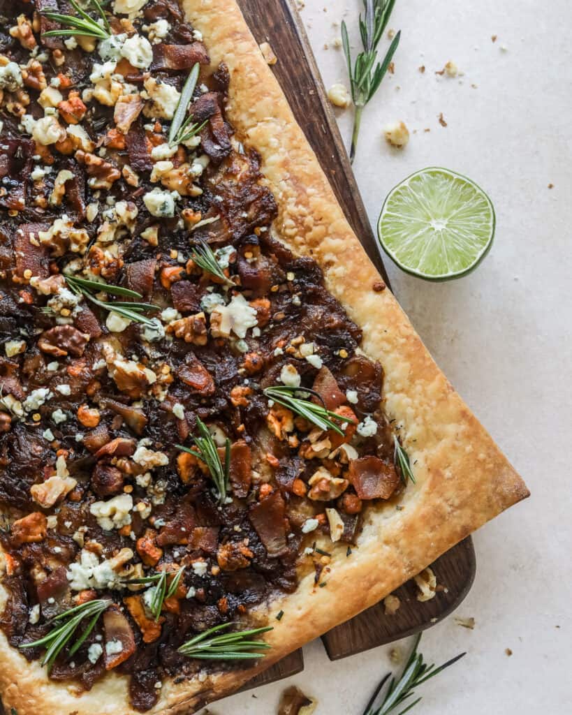 Caramelized Onion Puff Pastry with bacon and gorgonzola on a cutting board with rosemary leaves