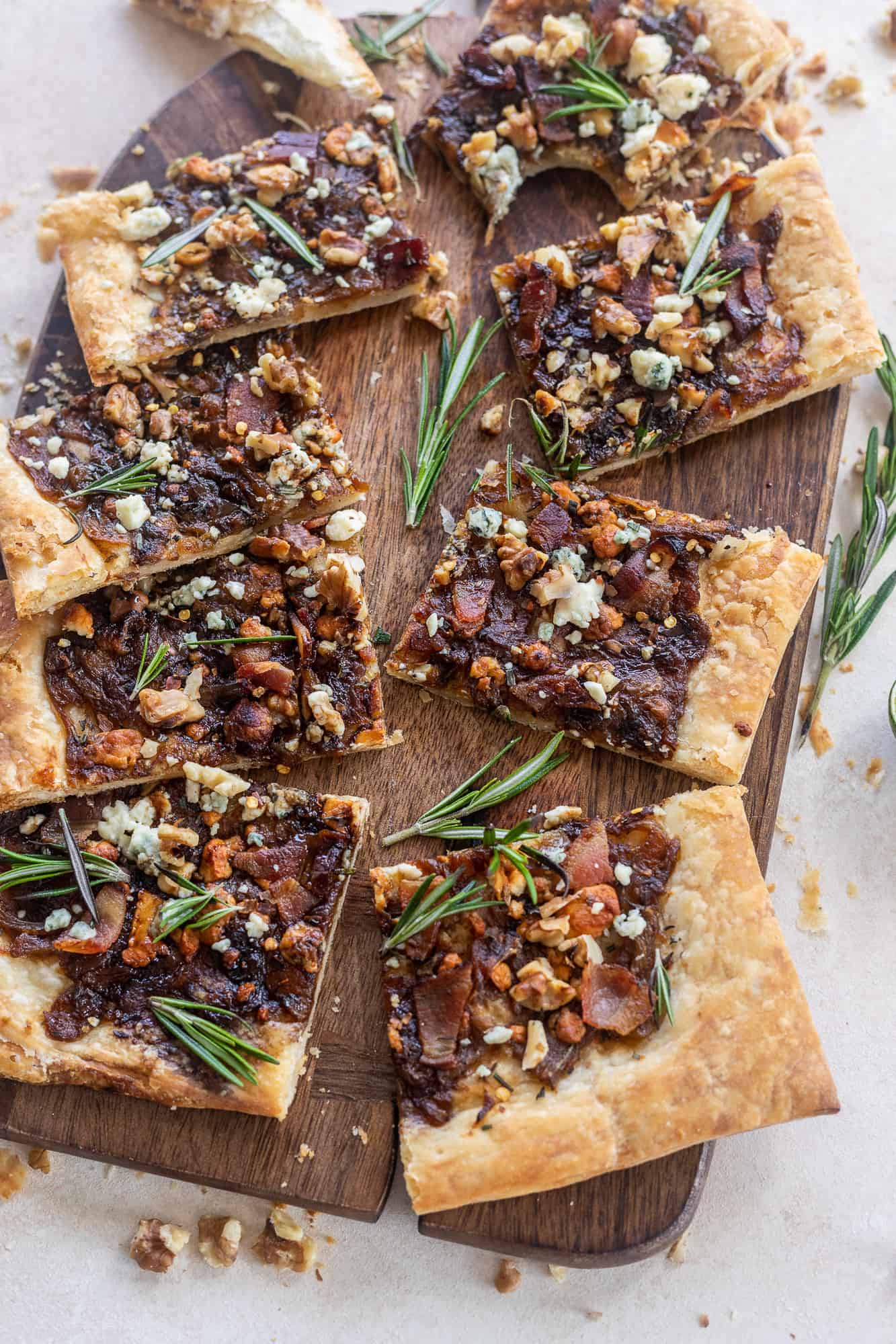 Caramelized Onion Puff Pastry with bacon and gorgonzola on a cutting board with rosemary leaves
