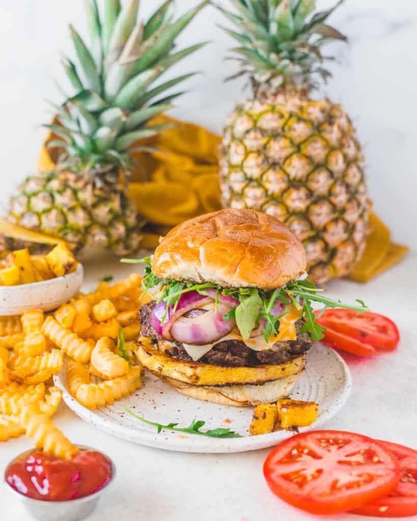 burger and fries on a plate with pineapples in the background