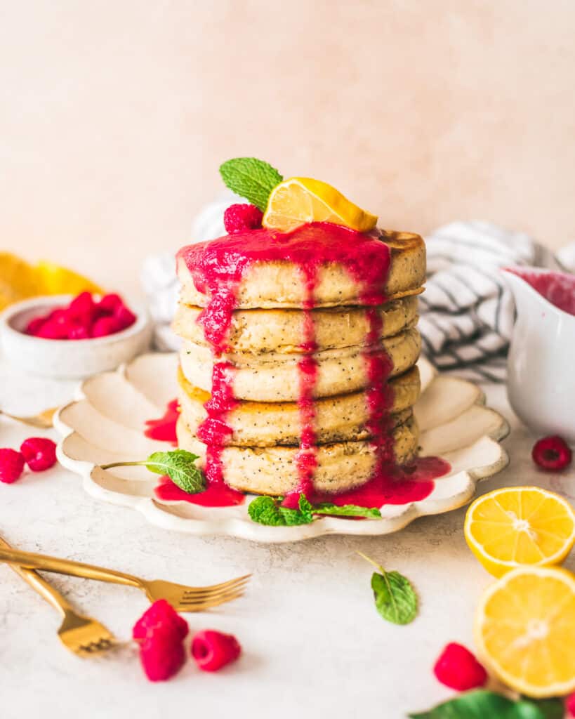 Lemon poppyseed pancakes on a plate with lemons and raspberries