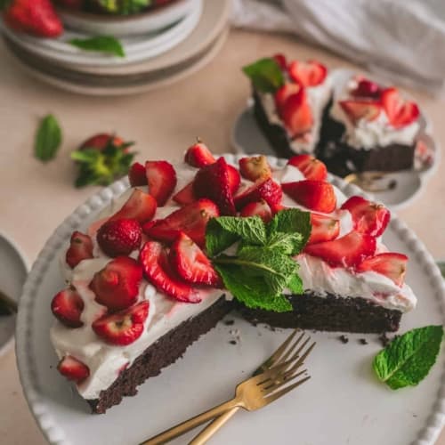 Strawberries and cream chocolate cake on a cake stand with forks