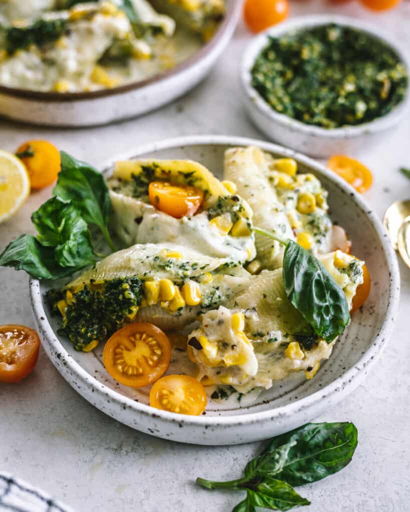 kale pesto and cheese stuffed shells in a baking dish with veggies around it
