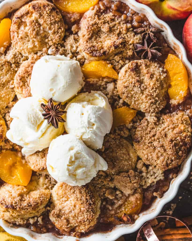 vegan peach cobbler with cinnamon streusel on a wooden surface with peaches and cloth around it
