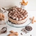 No Bake Tiramisu Cheesecake on a cake stand with lady fingers behind it