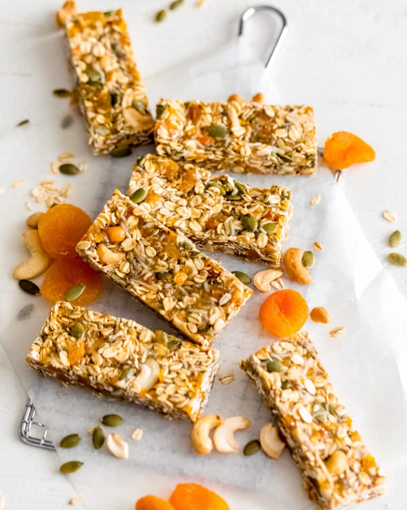 Apricot Coconut Cashew bars on a white surface with dried apricots and pumpkin seeds