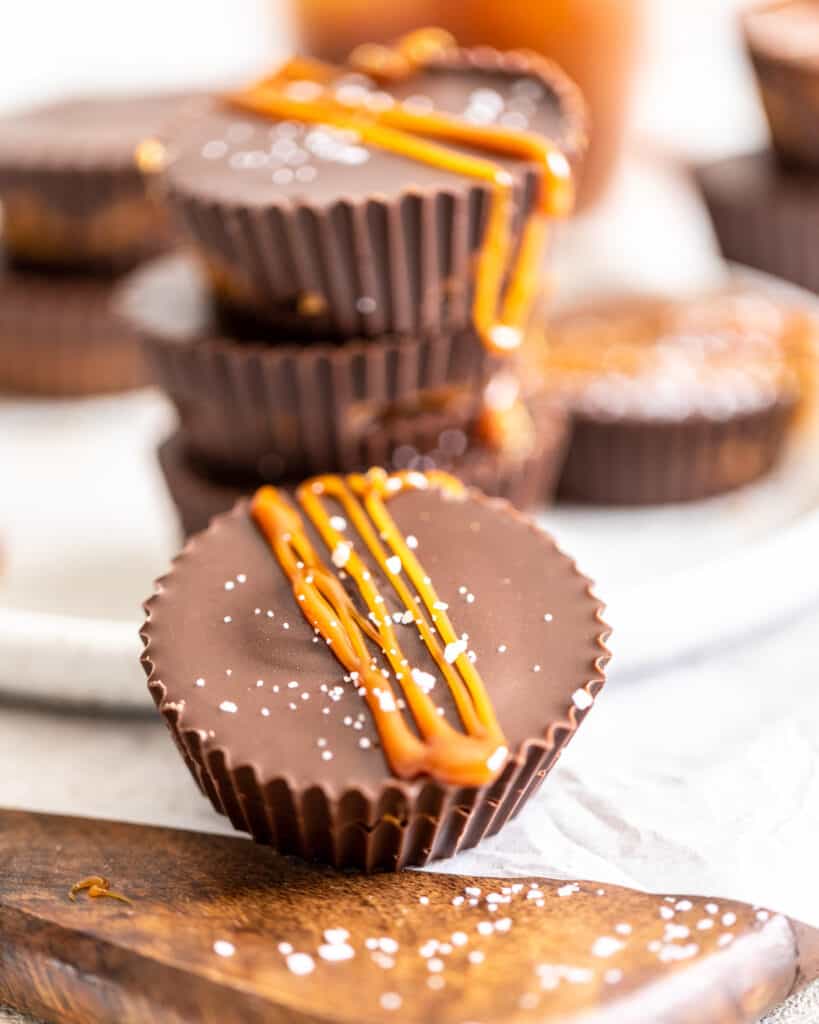 salted caramel peanut butter cups with caramel drizzled on top and more peanut butter cups in the background