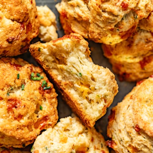 up close photo of cheddar biscuits with chives on a serving tray with one biscuit with a bite taken out of it.