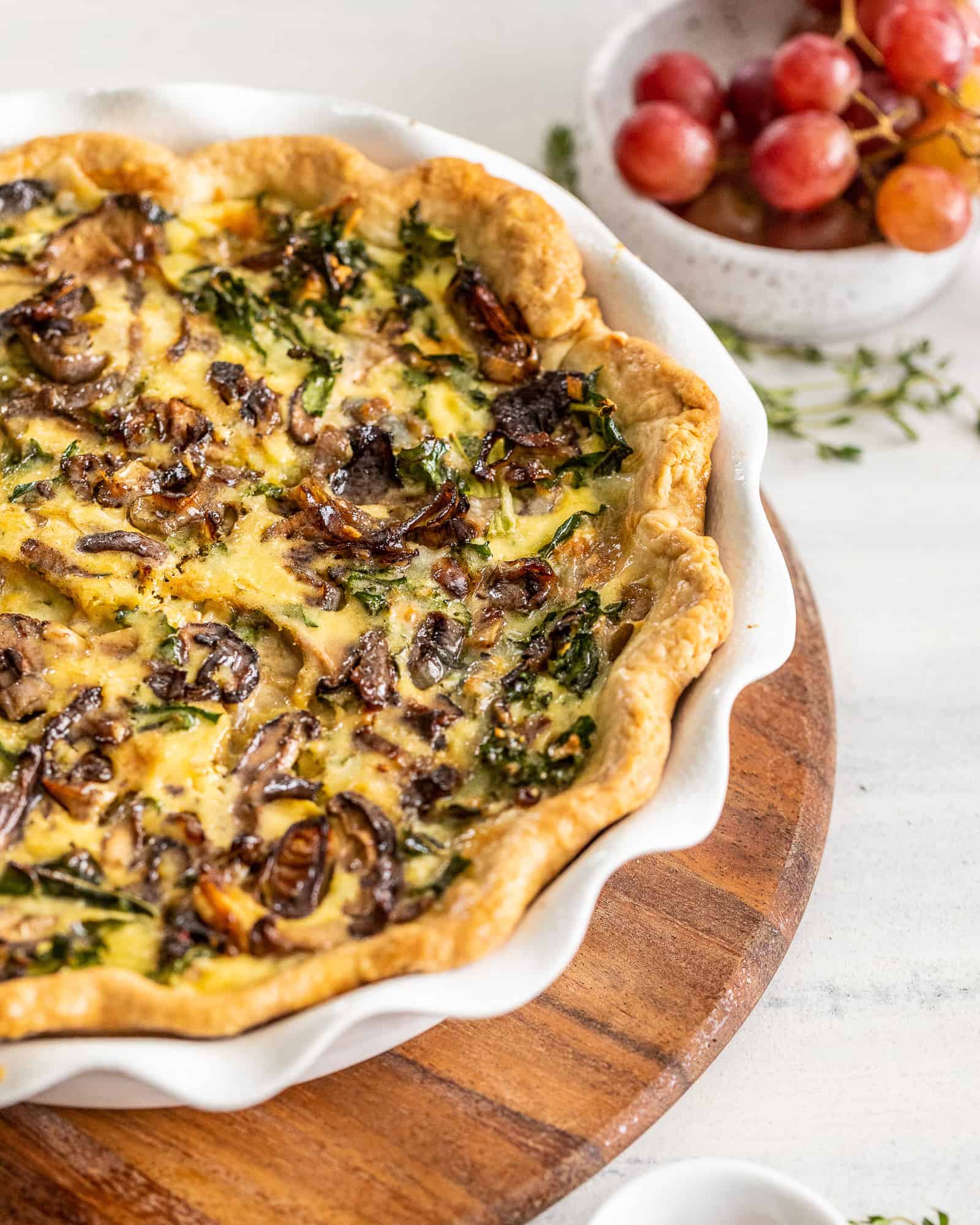 Close up view of a plated Kale and Mushroom Quiche and a bowl of tomatoes in the background