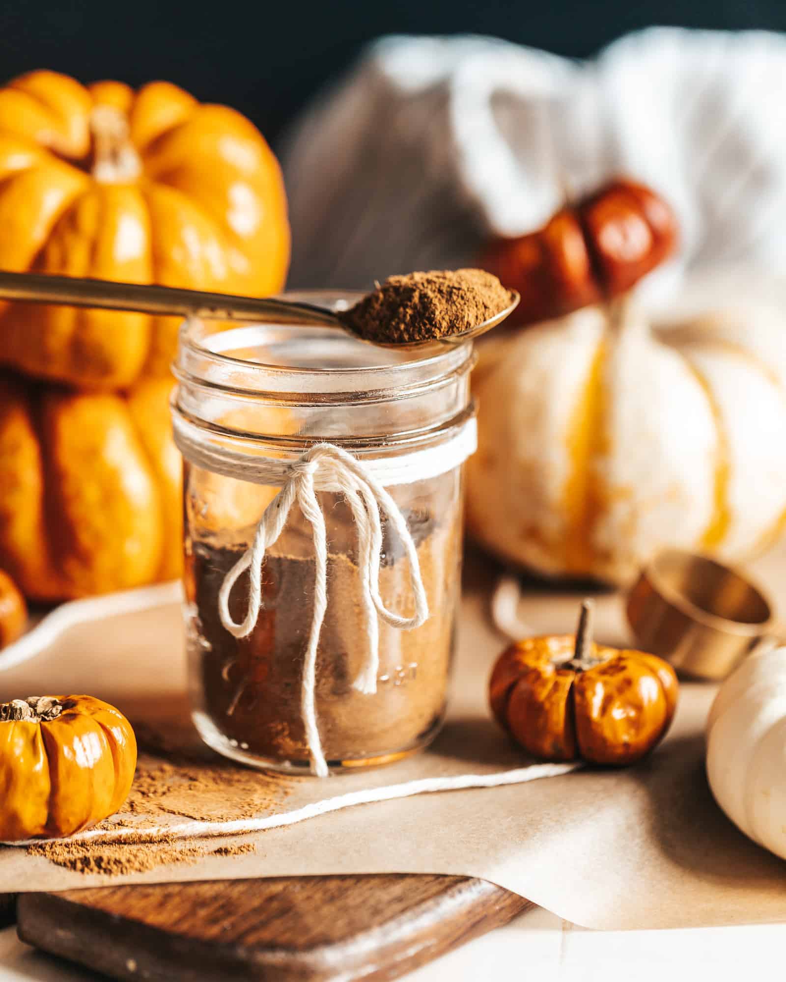 A jar of Homemade Pumpkin Spice with a spoonful on top and a variety of pumpkins in the background.