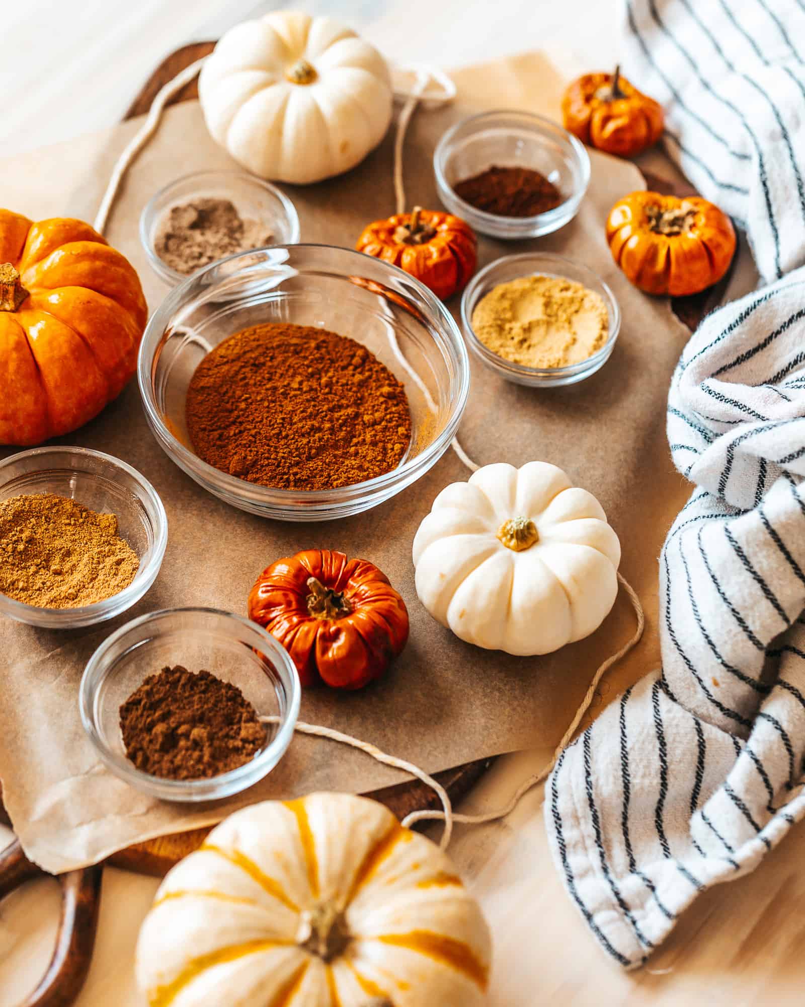 Overhead view of an assortment of the ingredients for the Spice recipe in glass bowls, along with an assortment of pumpkins and a striped blue and white cloth.