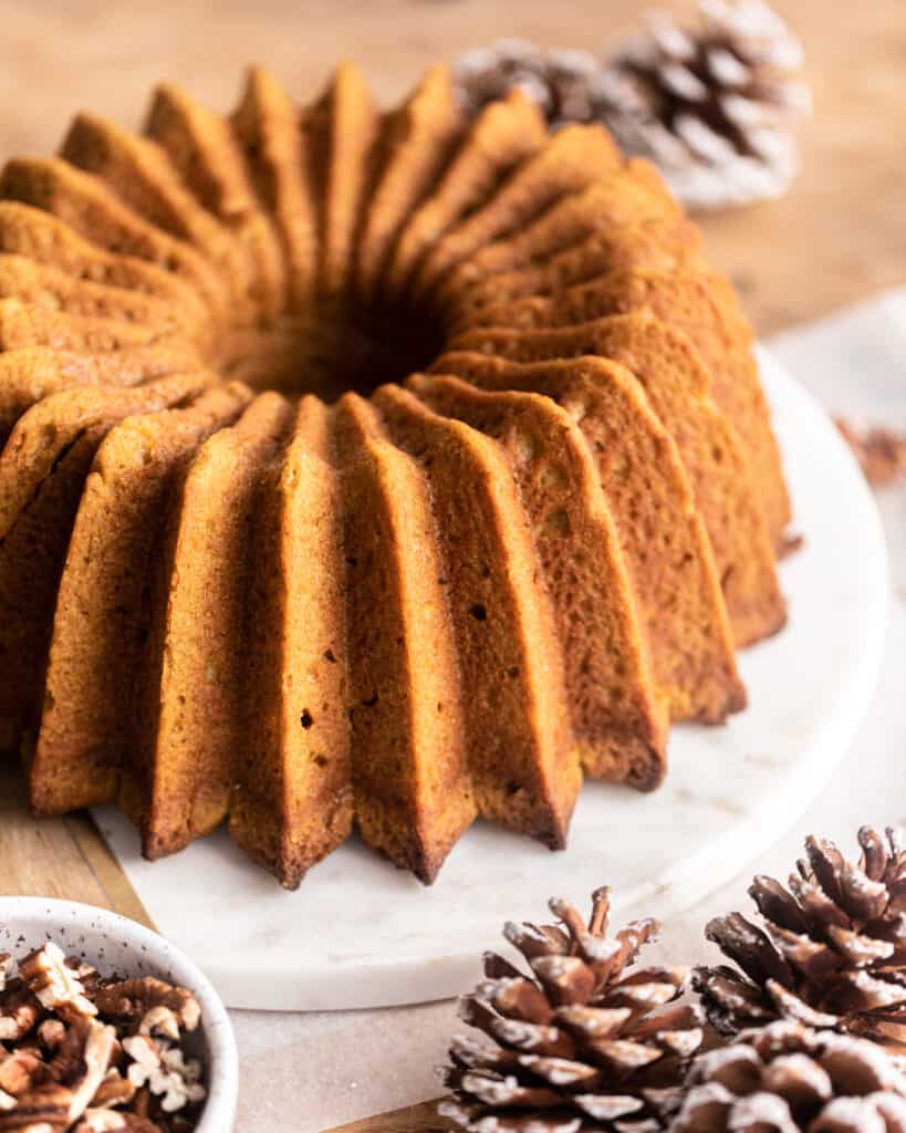 An unfrosted Pound Cake with a bowl of walnuts to the left and an assortment of frosted pine cones to the right and in the background.