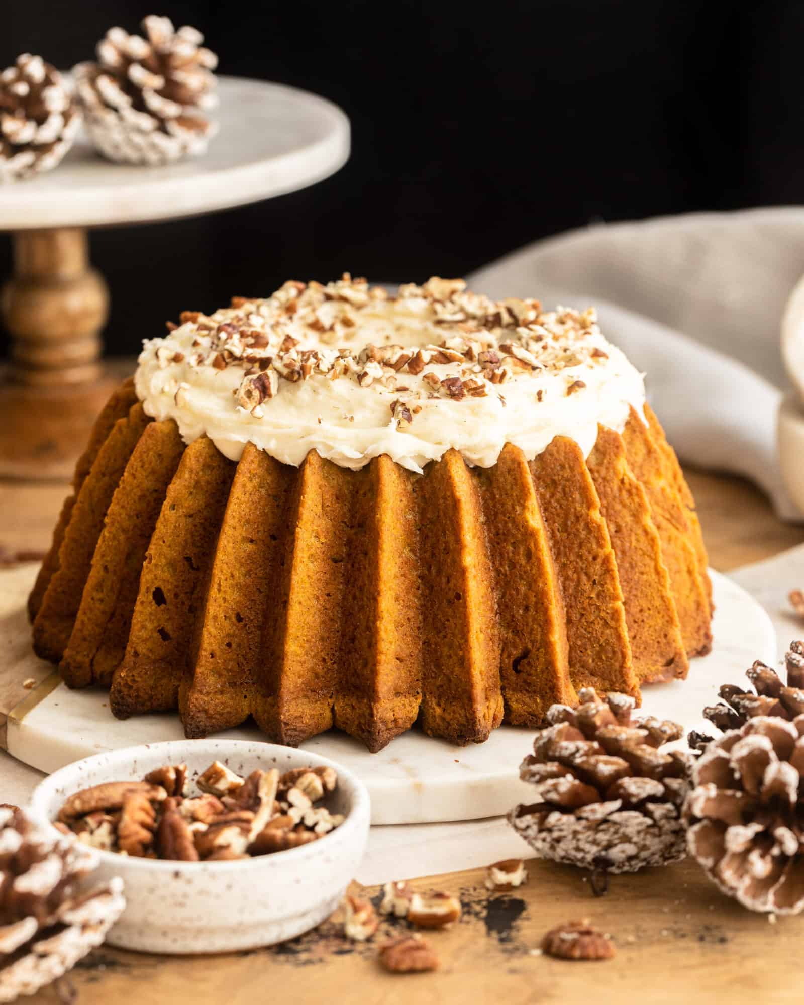 Sweet Potato Pound Cake with Cream Cheese Frosting on a platter surrounded by a small bowl of walnuts and frosted acorns.