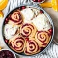 Cinnamon Rolls in a cake pan with cranberries around it on top of a dish cloth