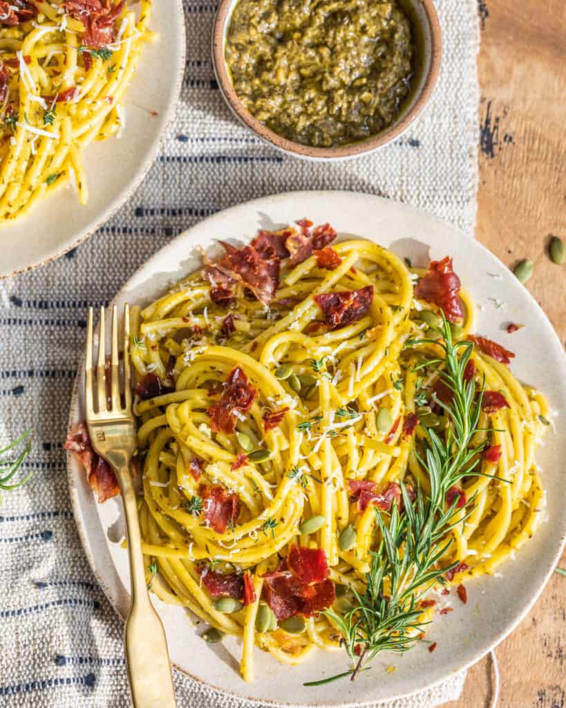 pesto carbonara with crispy prosciutto on a plate with a bowl of pesto next to it