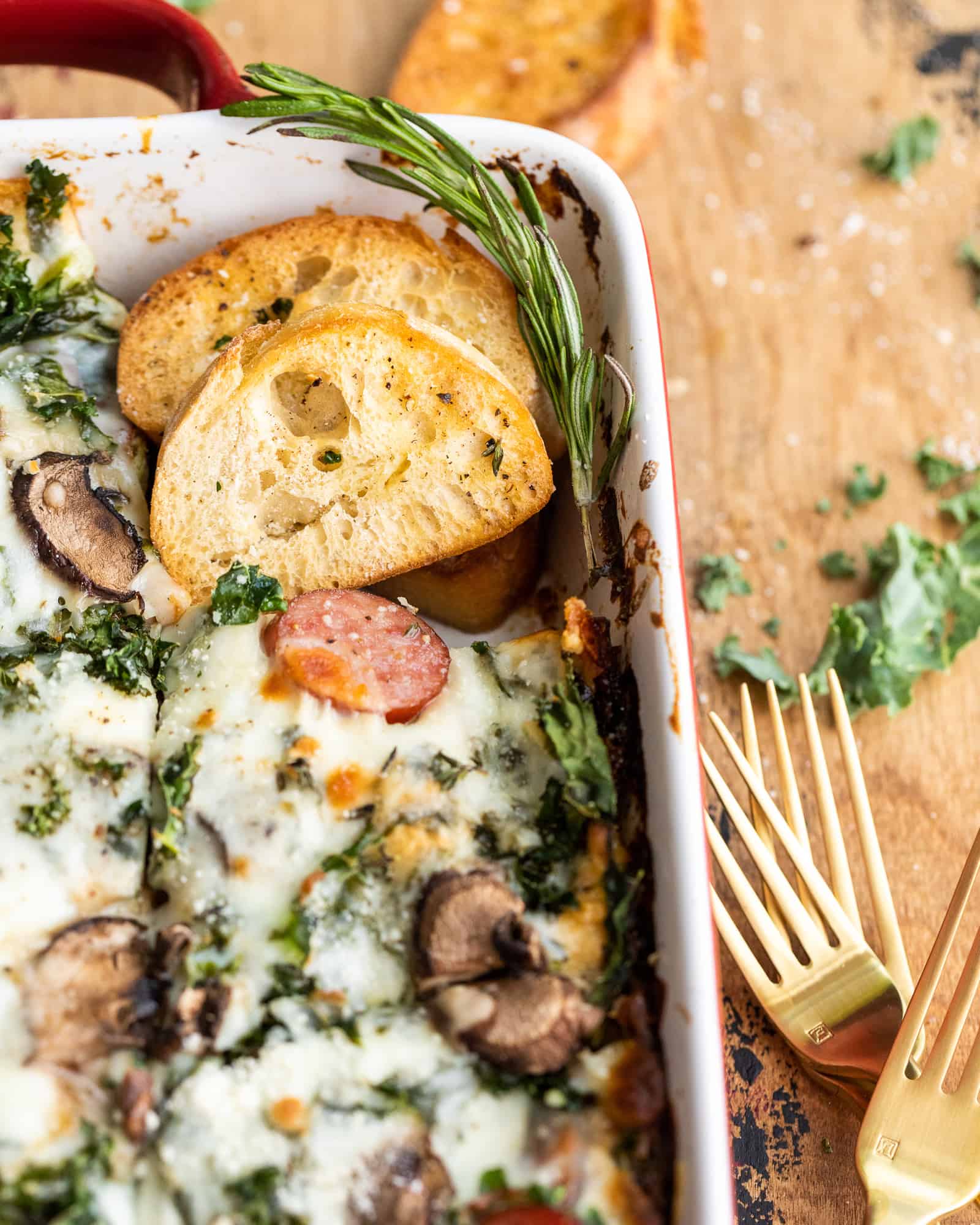 sausage kale and mushroom lasagna in a baking dish with a piece of bread
