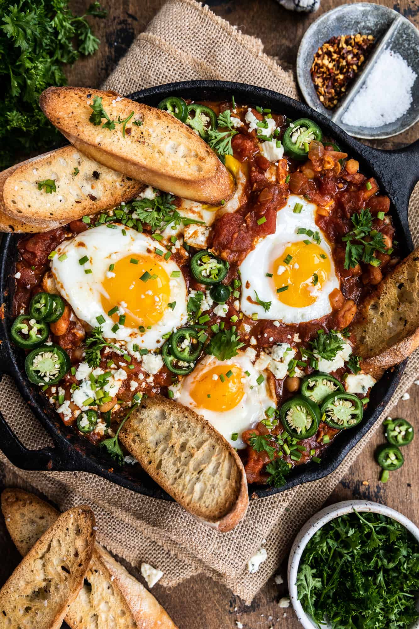 shakshuka in a cast iron skillet with sea salt red pepper and jalapenos in a bowl